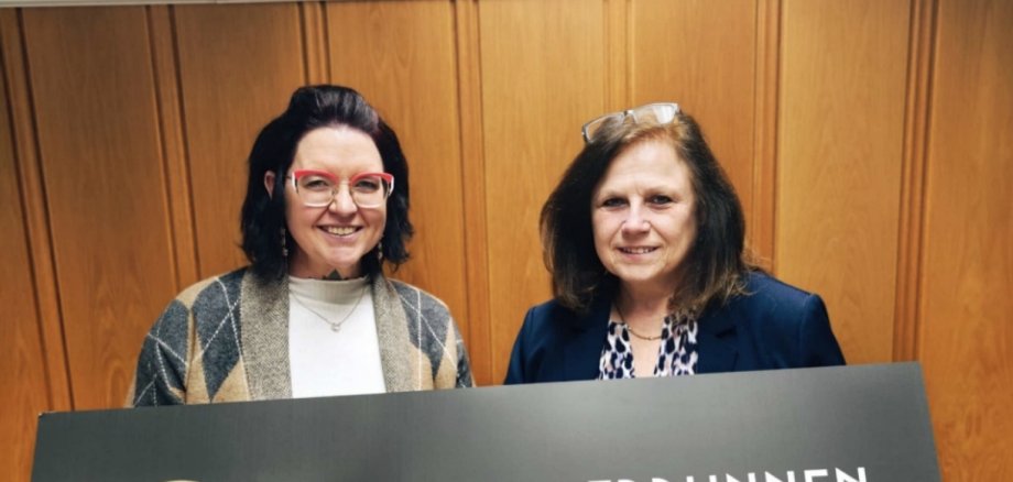 Michaela Rasch und Carmen Dietenhoven halten ein Schild mit dem neuen Logo hoch
