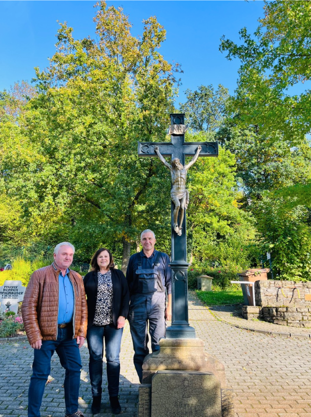 drei Menschen stehen vor einem restaurierten Friedhofskreuz